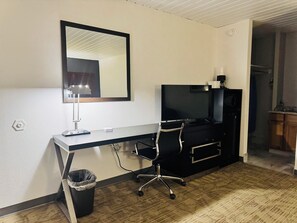 Et hotelværelse med skrivebord, stol, fjernsyn og en skraldespand.