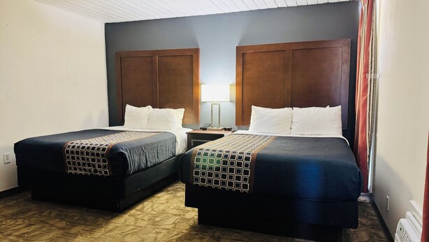 A hotel room with two beds, a nightstand, a lamp, and a window with curtains.