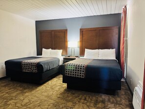 A hotel room with two beds, a nightstand, a lamp, and a window with curtains. - Alamo Inn & Suites (Gillette)