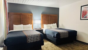 A hotel room with two beds, a nightstand, a lamp, and a framed picture on the wall.