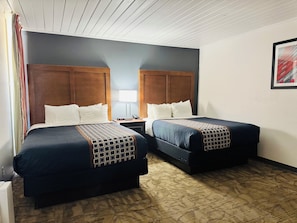 A hotel room with two beds, a nightstand, a lamp, and a framed picture on the wall.