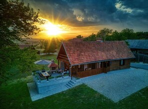 Eine rustikale Holzhütte mit rotem Dach, einer Terrasse mit Sitzgelegenheiten und einer Einfahrt mit Schotterbefestigung.
