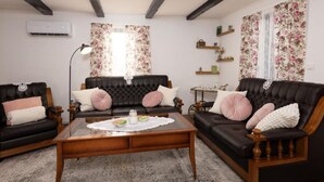 Een woonkamer met twee zwarte leren banken, een houten salontafel en bloemen gordijnen.