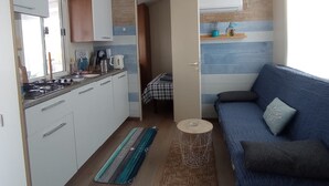 Pieni, käytännöllinen keittiö, jossa on kaasuliesi, valkoiset kaapit ja siniraidallinen seinä.