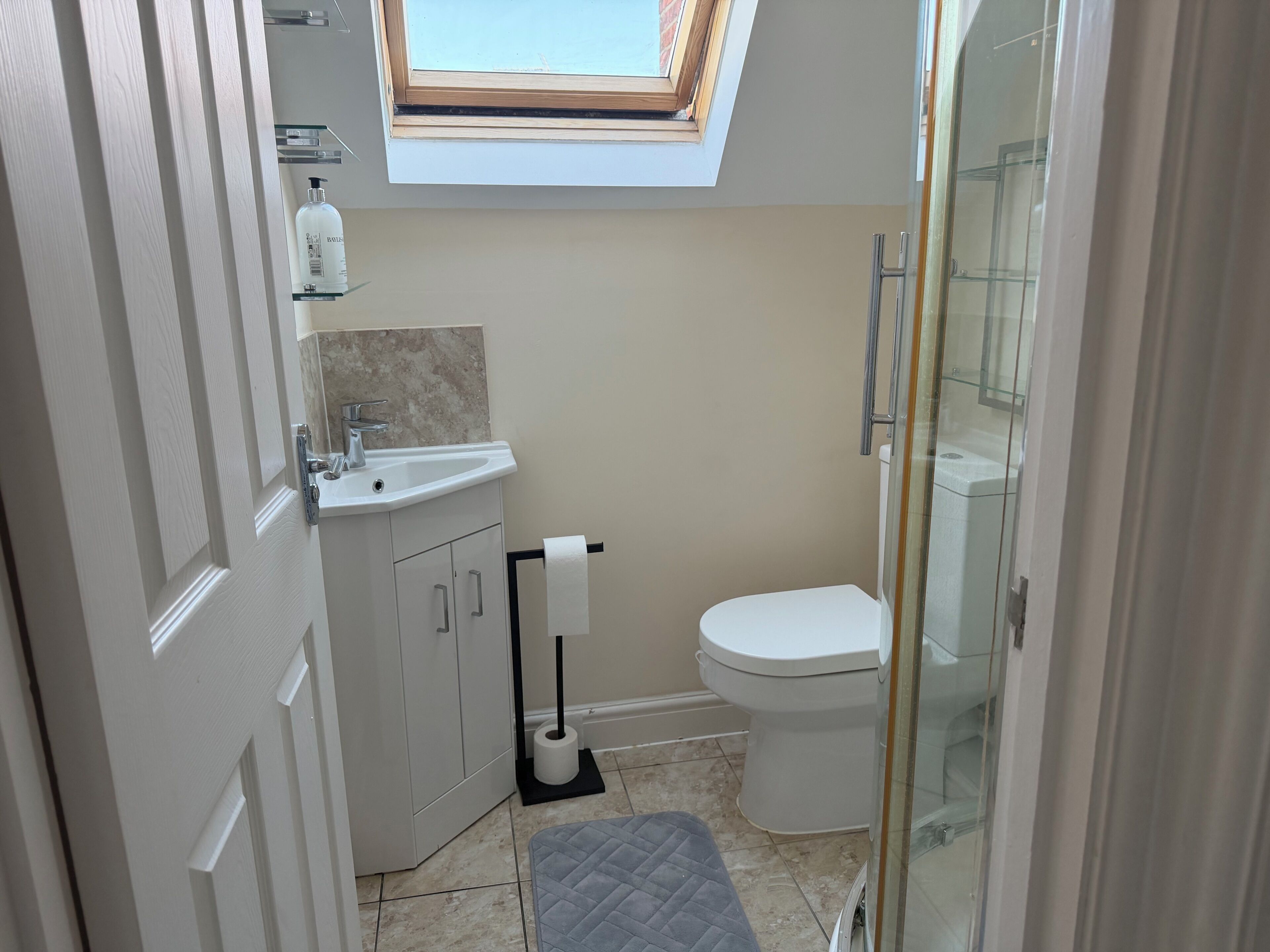 A compact bathroom with a skylight, a toilet, a sink, and a shower area.