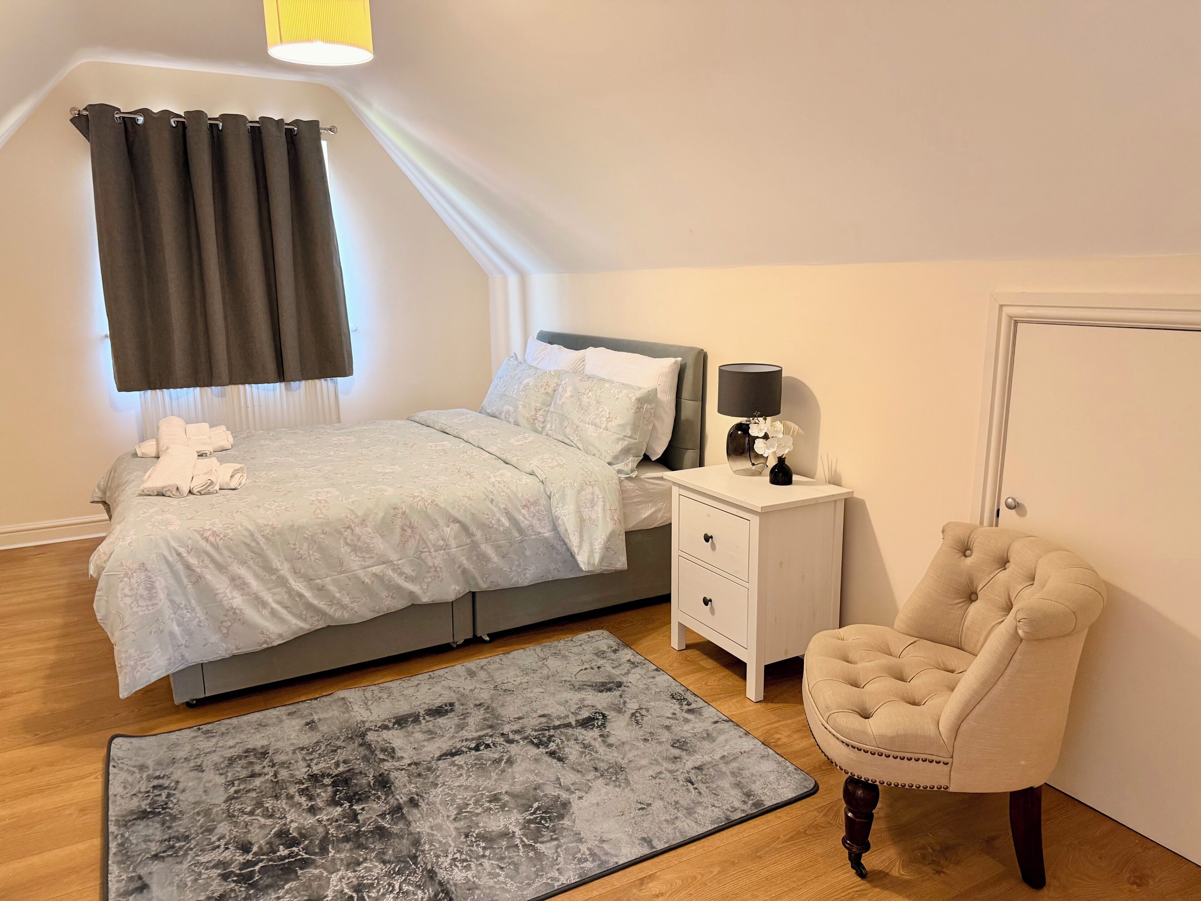 A bedroom with a bed, bedside table, lamp, chair, and a rug.