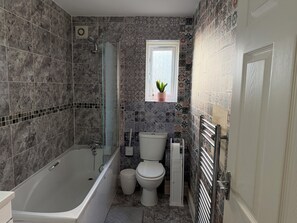 Une salle de bain avec une baignoire, des toilettes, une douche et une fenêtre agrémentée d’une plante.