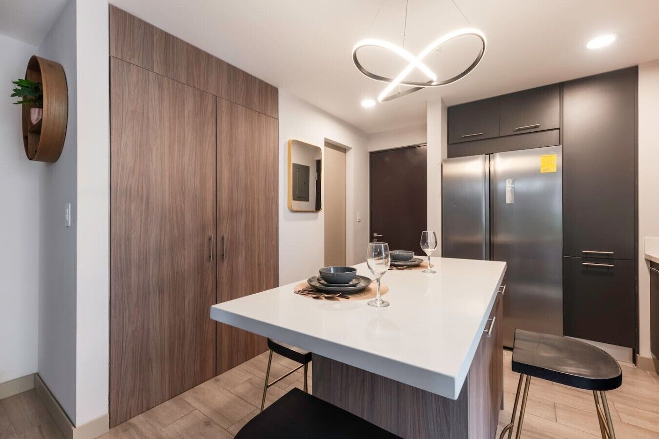 Une cuisine moderne dotée d’un îlot central, de meubles de couleur sombre et d’un réfrigérateur en acier inoxydable.