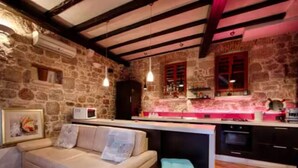 A cozy room with a stone wall, a white sofa, a kitchen area with a pink countertop, and a wooden ceiling. - Four Bedroom House with Terrace (Komiza)