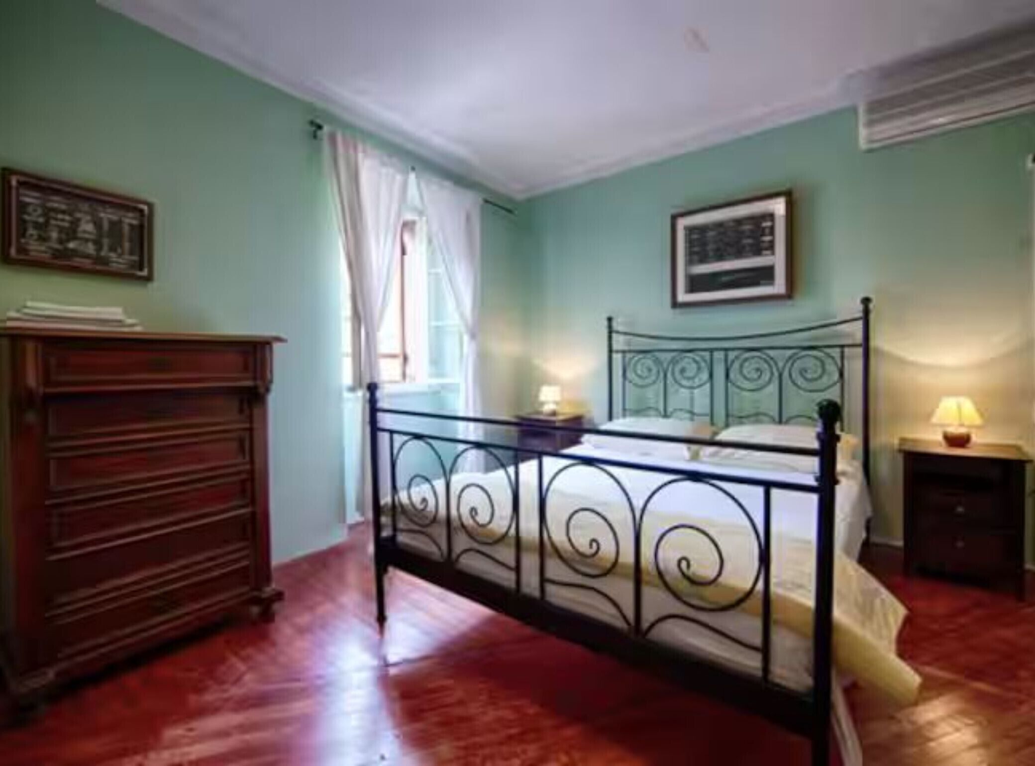 A room with a bed, a dresser, a window with curtains, and a picture on the wall.