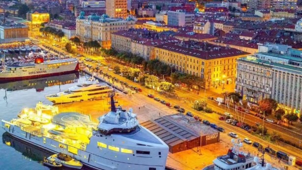 Una marina con varios yates amarrados, un edificio grande con una cúpula y una calle concurrida con edificios al fondo.