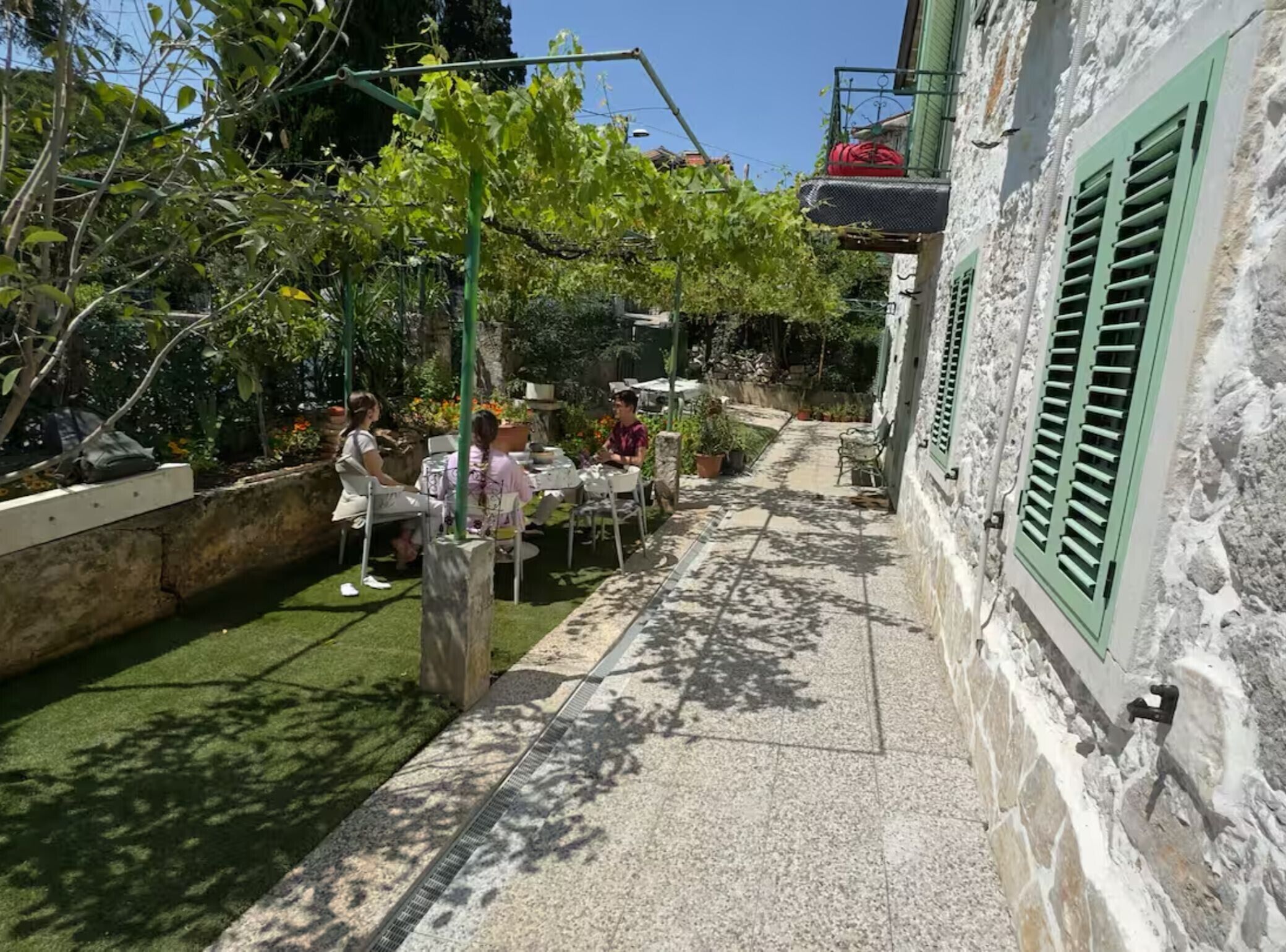 An outdoor patio with tables and chairs, surrounded by greenery and a stone wall.