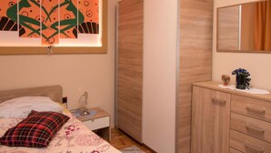 Un dormitorio con cama, mesita de noche, lámpara, cómoda, espejo y una obra de arte en la pared.