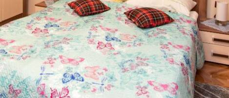A bed with a floral and butterfly-patterned bedspread, two pillows, and a bedside table with a lamp.