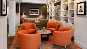 Ein modernes Wohnzimmer mit orangefarbenen Sesseln, einem Sofa, einem Couchtisch und einem Bücherregal voller Bücher und Dekoration.