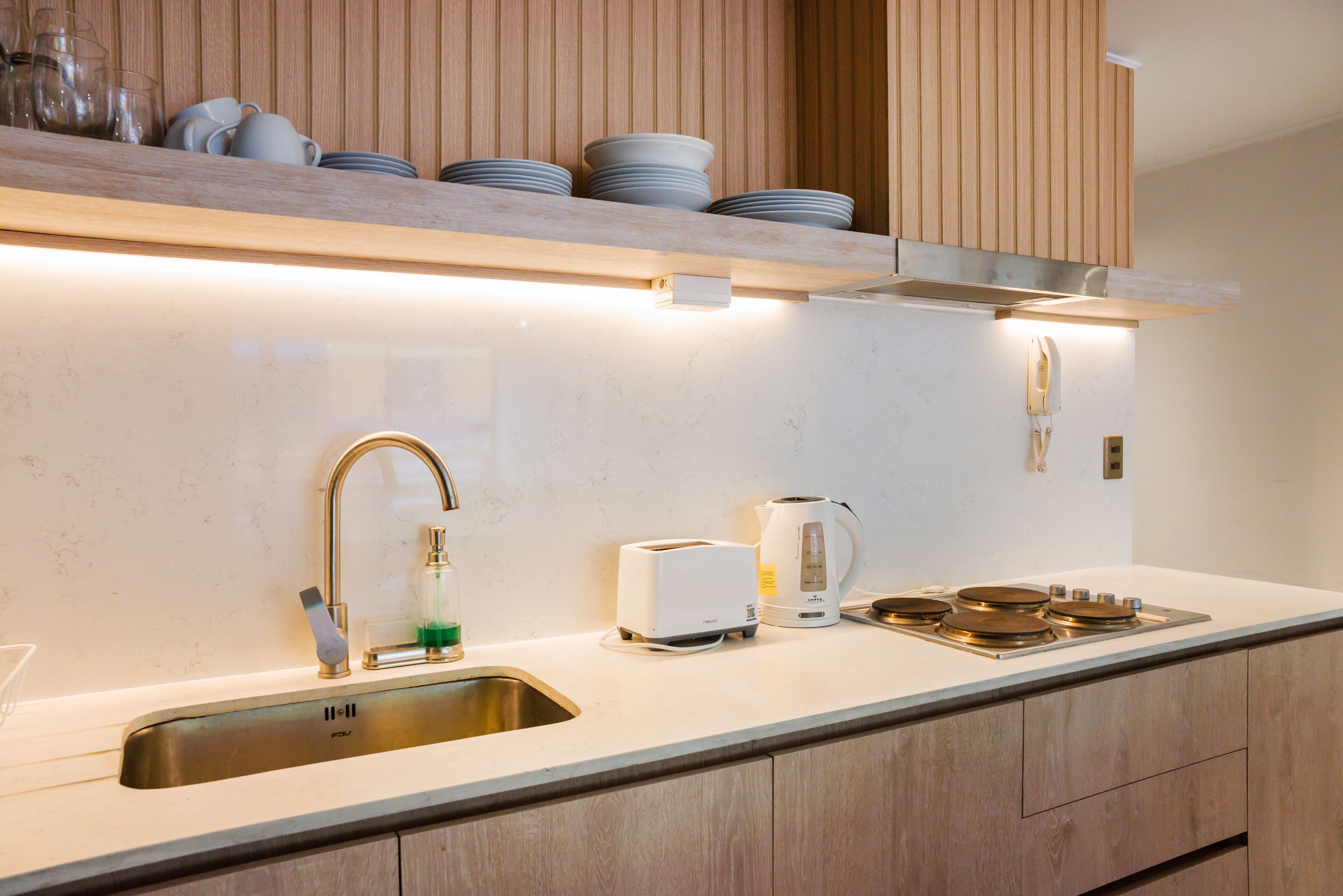 A modern kitchen with a stainless steel sink, a toaster, a kettle, and wooden cabinets.