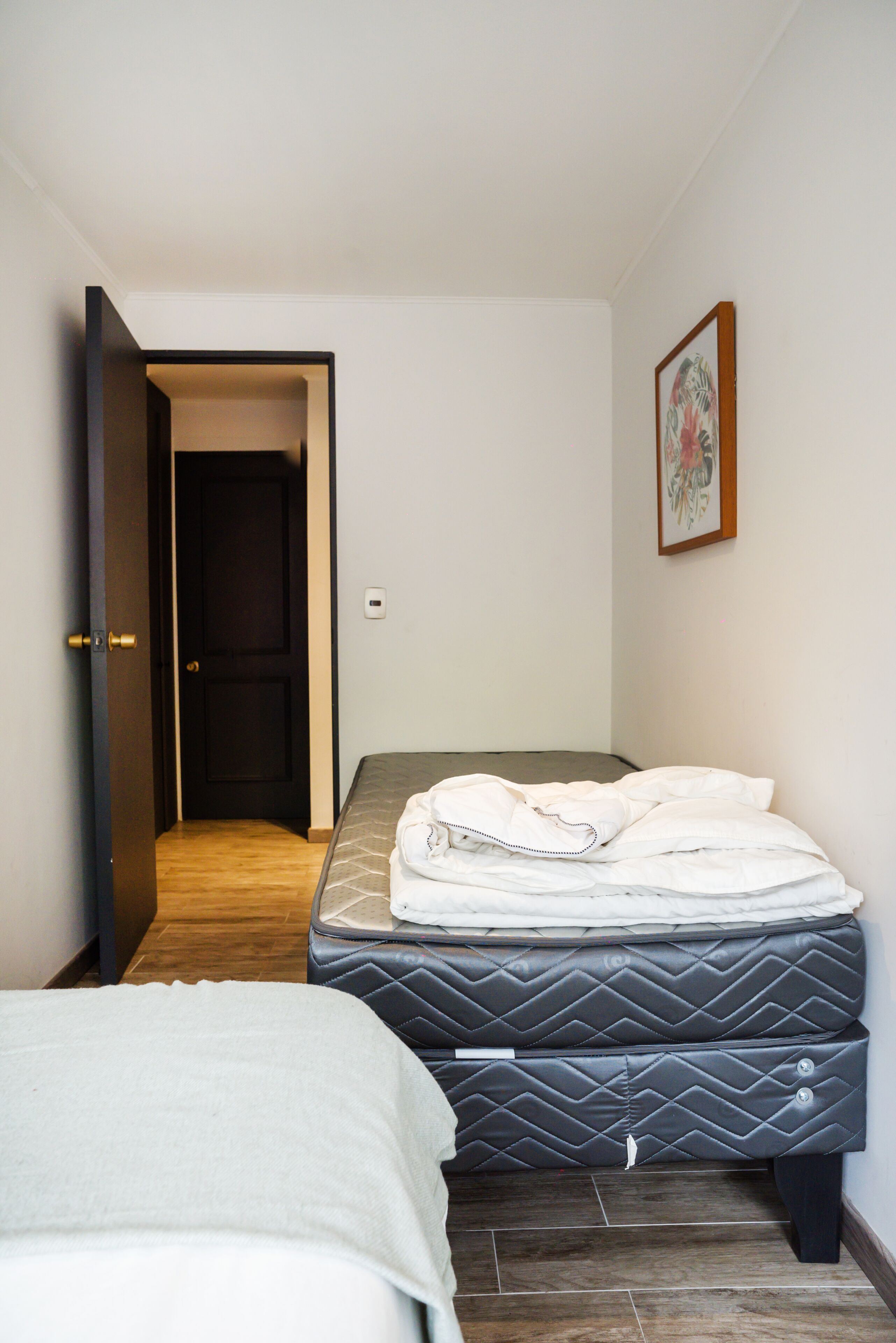 Un dormitori amb un llit, una taula de nit i una porta que dona a una altra habitació.