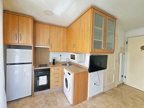 A compact kitchen with wooden cabinets, a built-in oven, a microwave, a washing machine, and a TV. - Ático A - Cartagena Centro histórico by Interhome (Cartagena)