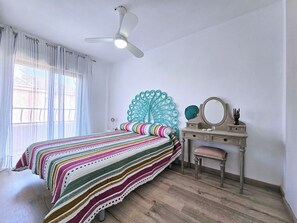 Une chambre à coucher comprenant un lit, une coiffeuse avec un miroir, une tête de lit décorée de motifs de paon et un ventilateur de plafond.