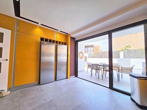 Une cuisine moderne équipée de deux réfrigérateurs en acier inoxydable, un coin repas avec une table et des chaises, et une grande porte-fenêtre coulissante donnant sur un patio extérieur.