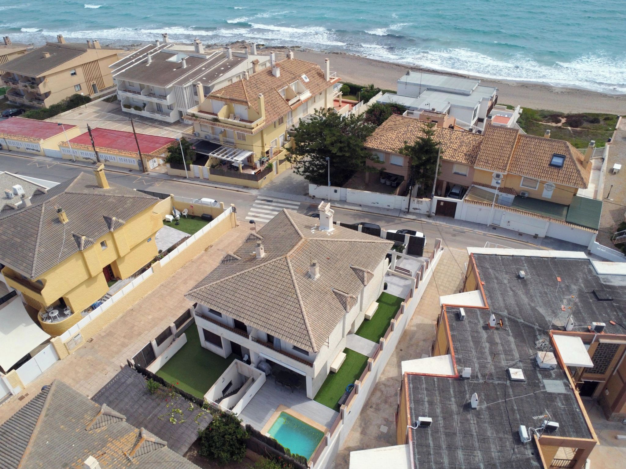 Vista aérea de una zona residencial costera con casas, una piscina y una playa.