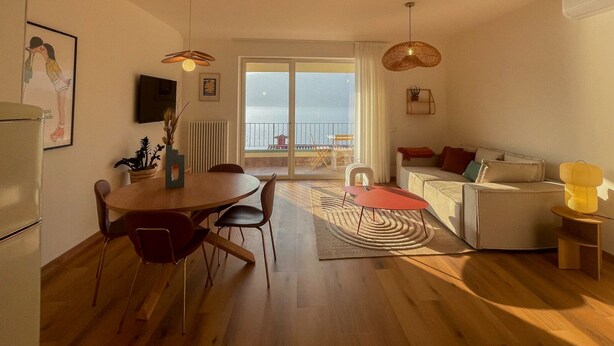 A modern living room with a dining area, a sofa, a small table, and a view of the sea through large windows. - 2-bedroom apartment with lakeview in beautiful Brenzone sul Garda with AC (Brenzone sul Garda)