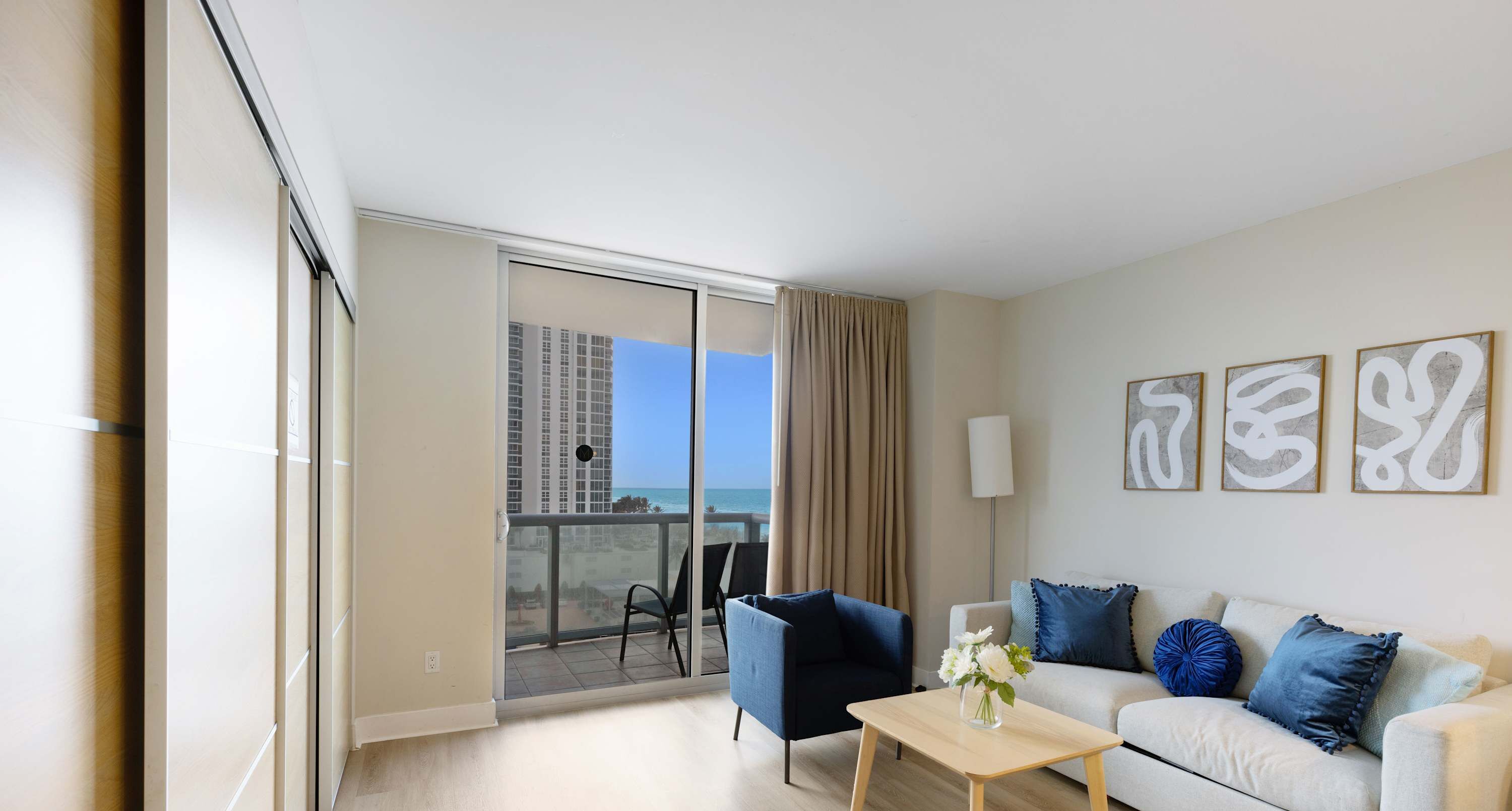A modern hotel room with a balcony, a sofa, a coffee table, and artwork on the wall.