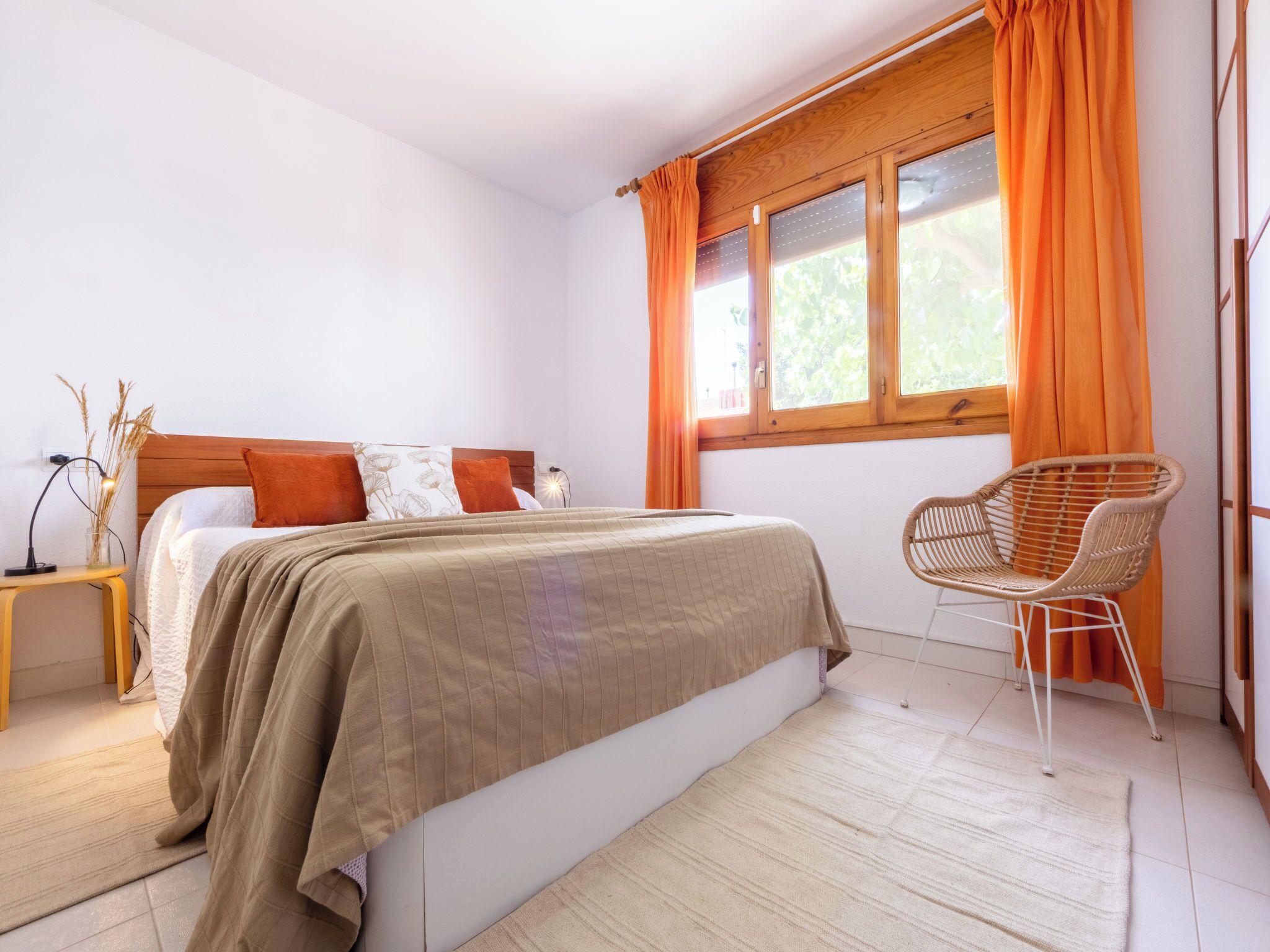 Une chambre à coucher avec un lit, une chaise, une table de chevet et une fenêtre avec des rideaux.