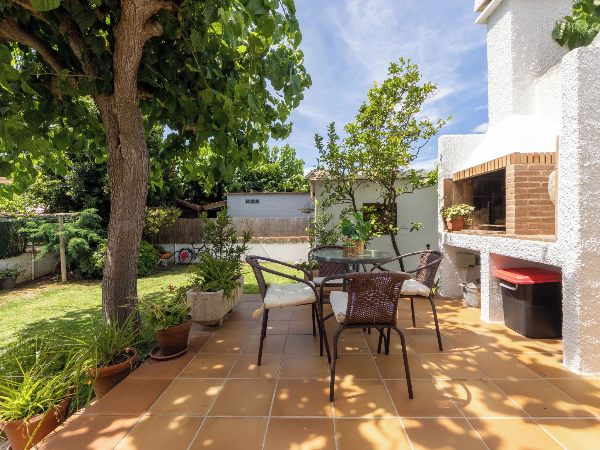 Eine Terrasse mit Tisch und Stühlen, umgeben von Kübelpflanzen und einem Baum.