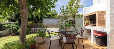 A patio with a table and chairs, surrounded by potted plants and a tree.