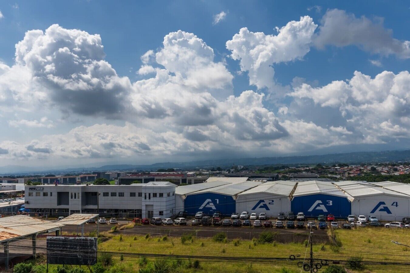A large industrial facility with multiple warehouses labeled A1, A2, A3, and A4, surrounded by parked cars and a clear sky with clouds.