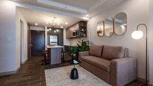 Ein modernes Wohnzimmer mit einer Couch, einem Couchtisch und einer Stehlampe. Es gibt eine Küchenzeile mit einem Kühlschrank und einem Esstisch.