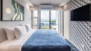 Ein modernes Hotelzimmer mit einem großen Bett, einem Flachbildfernseher und Blick auf die Stadtlandschaft durch das Fenster.