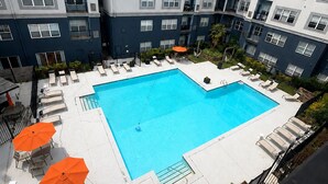 Ein Pool auf dem Dach mit Liegestühlen und Sonnenschirmen, umgeben von einem mehrstöckigen Gebäude mit Balkonen.