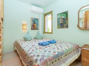 Une chambre avec un lit, deux oreillers, une lampe fixée au mur, un tableau, un miroir et un appareil de climatisation.
