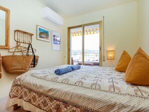 A bedroom with a bed, a hanging basket, a wall-mounted air conditioner, and a view through a glass door. - Vacation home Claudi by Interhome (Tossa de Mar)