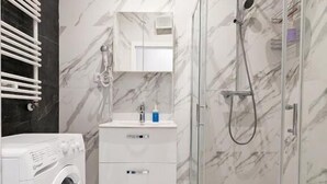 A modern bathroom with a glass shower enclosure, a built-in washing machine, and a marble-tiled floor. - Livin Apart A3 (Warszawa)