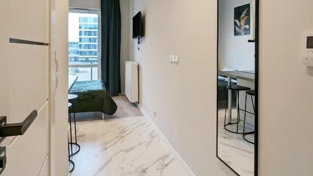 A hallway with a marble floor, a bed, a table, and a chair in the background. - Livin Apart A3 (Warszawa)