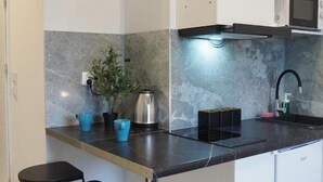 A modern kitchen with a marble backsplash, a microwave, a kettle, and two bar stools. - Livin Apart A3 (Warszawa)