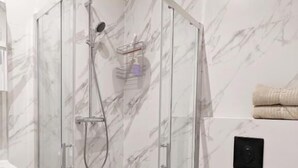 A glass-enclosed shower with a handheld showerhead, a white toilet, and marble-patterned walls. - Livin Apart A3 (Warszawa)