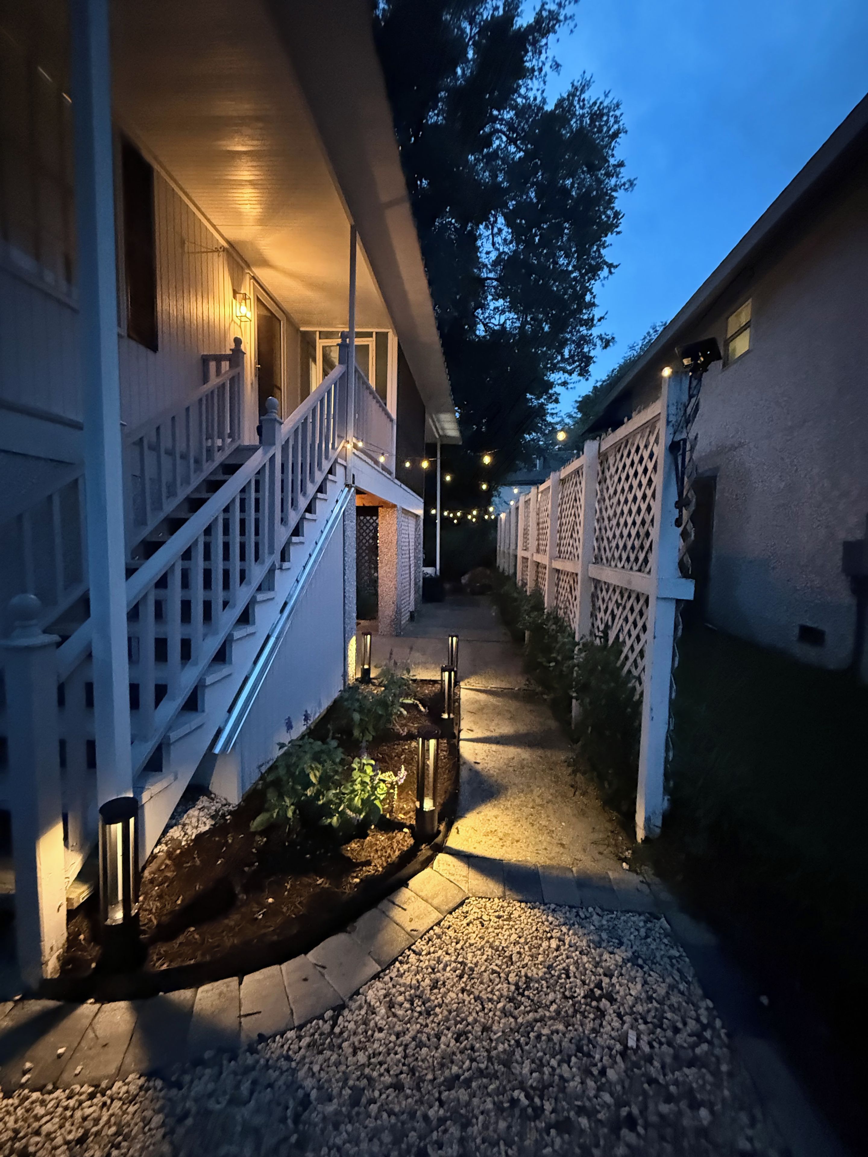 A pathway leading to a building with a staircase and a covered porch area.