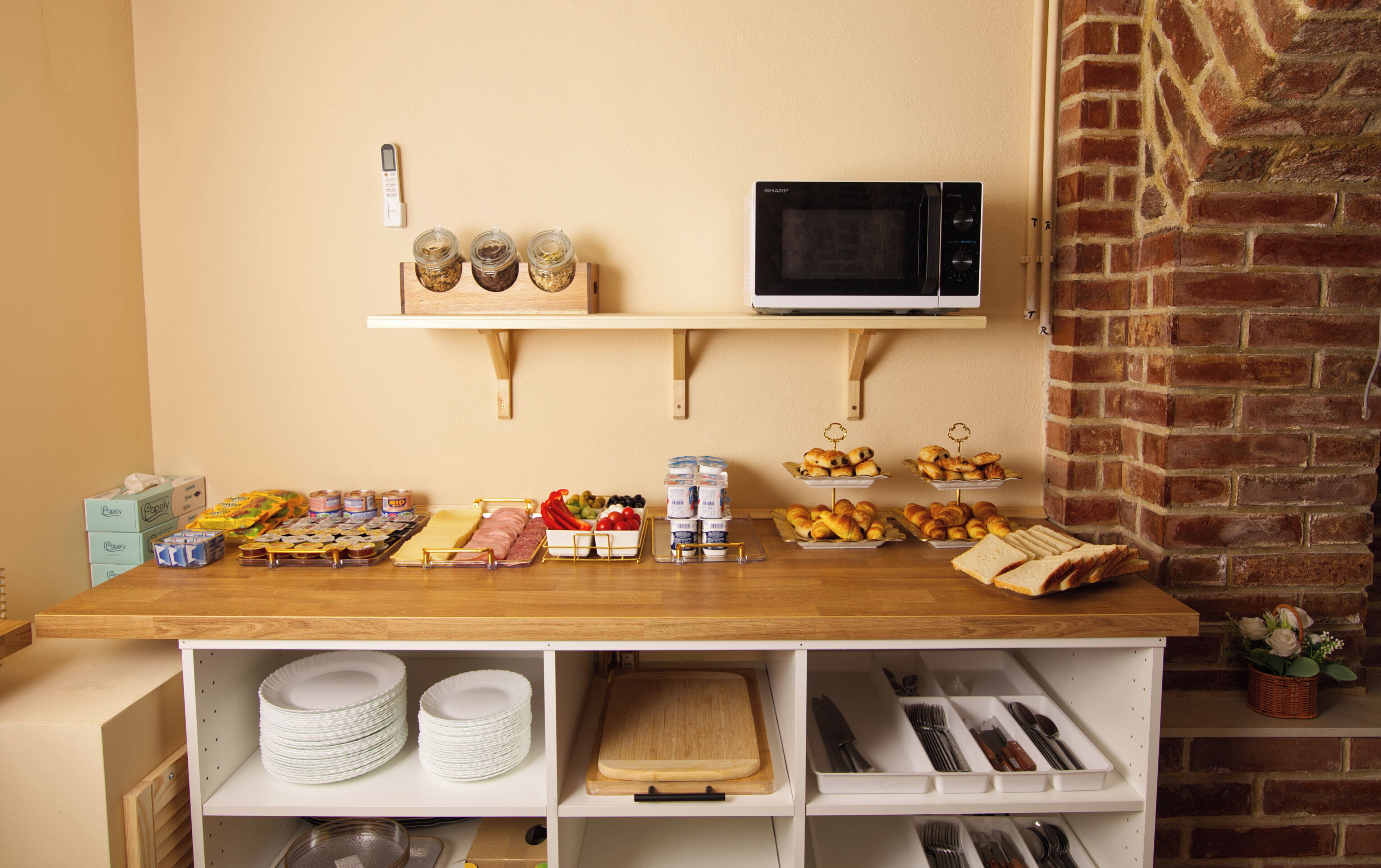 Una encimera de cocina con alimentos, un microondas y estantes con platos y cubiertos.