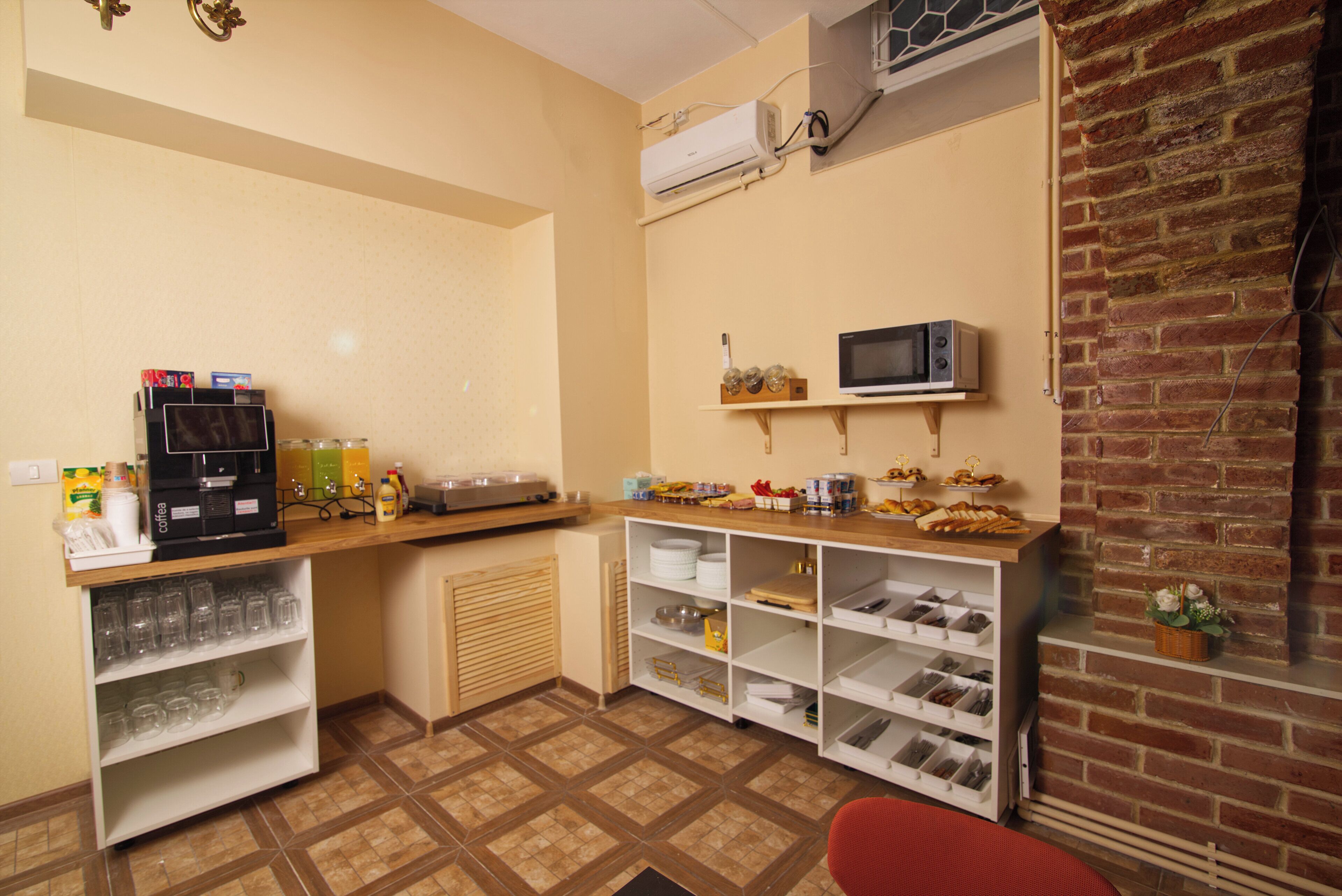 Una cocina con cafetera, repisas con cristalería, microondas y pared de ladrillo.