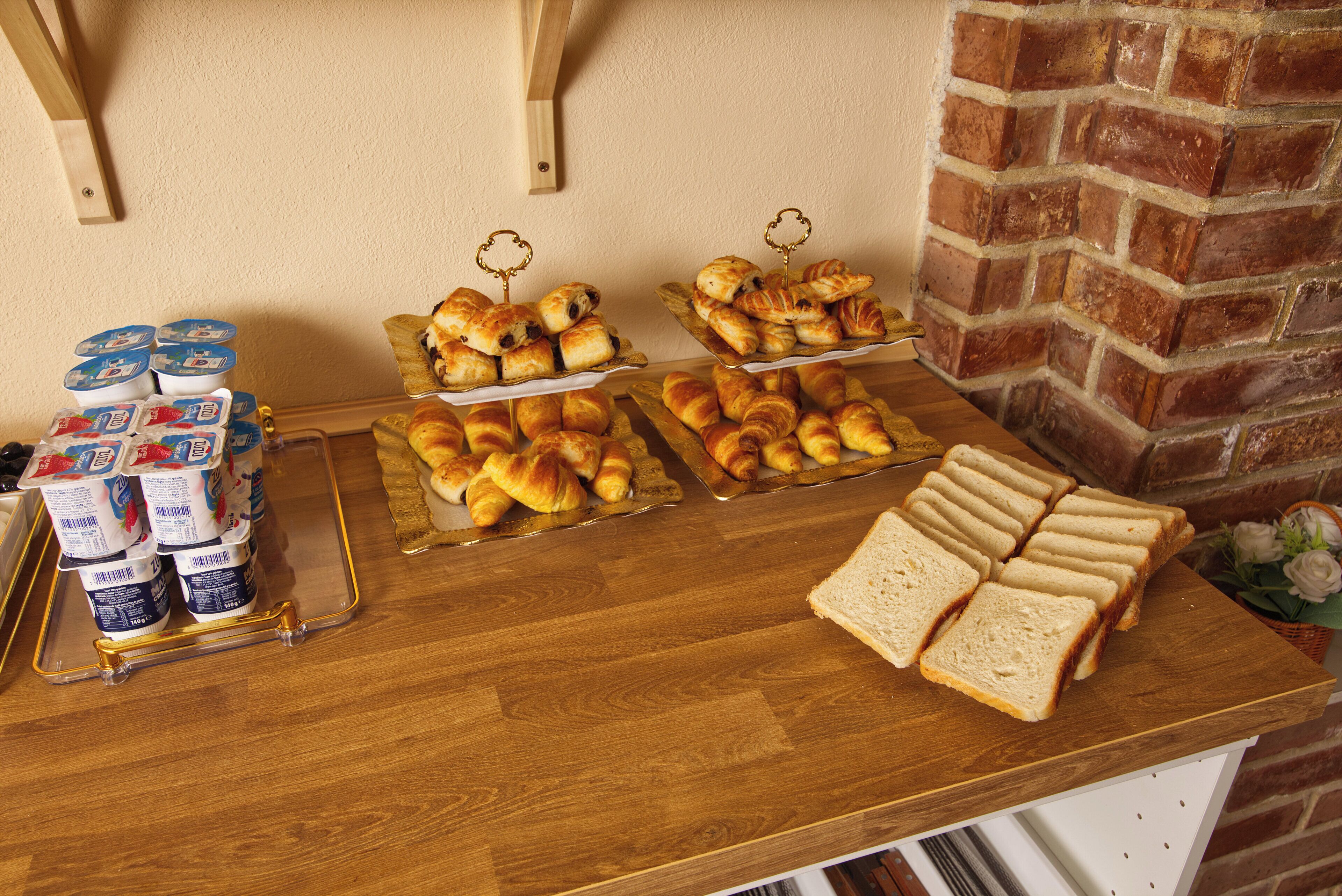 A breakfast buffet with pastries, bread, and yogurt on a wooden table.