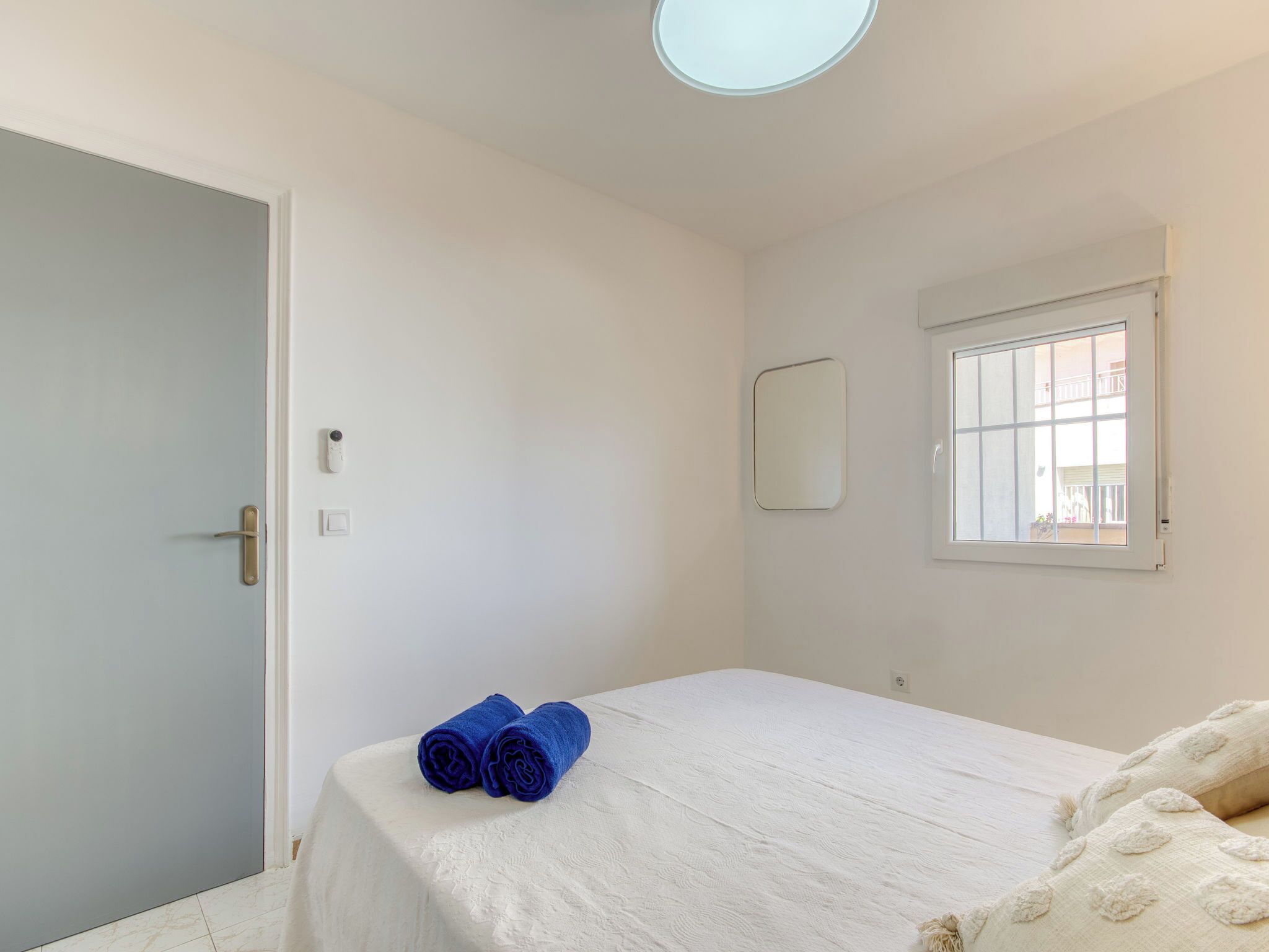 Un dormitorio con cama, puerta, ventana y espejo fijado a la pared.