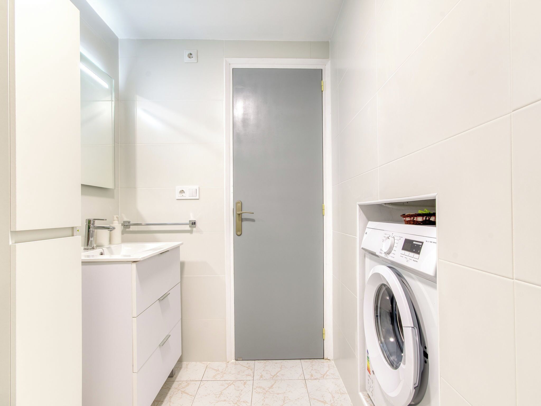 A compact laundry room with a washing machine, a sink, and a door.