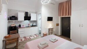 Quarto moderno com cama, mesas de cabeceira, escrivaninha e uma kitchenette.