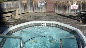 A hot tub with a view of the ocean, wooden buildings, and a sign indicating pool and spa hours. - Oceanfront 2/2 Condo w/ Panoramic Views on Del Monte Beach (Monterey)