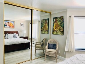 A bedroom with a bed, a chair, a large mirror, and artwork on the walls. - Oceanfront 2/2 Condo w/ Panoramic Views on Del Monte Beach (Monterey)