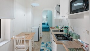 A compact kitchen with a microwave, sink, and small refrigerator. There is a dining table with chairs and a blue sofa in the background. - Apartment 'A casa re nonni' with Balcony, Wi-Fi and Air Conditioning (Naples)